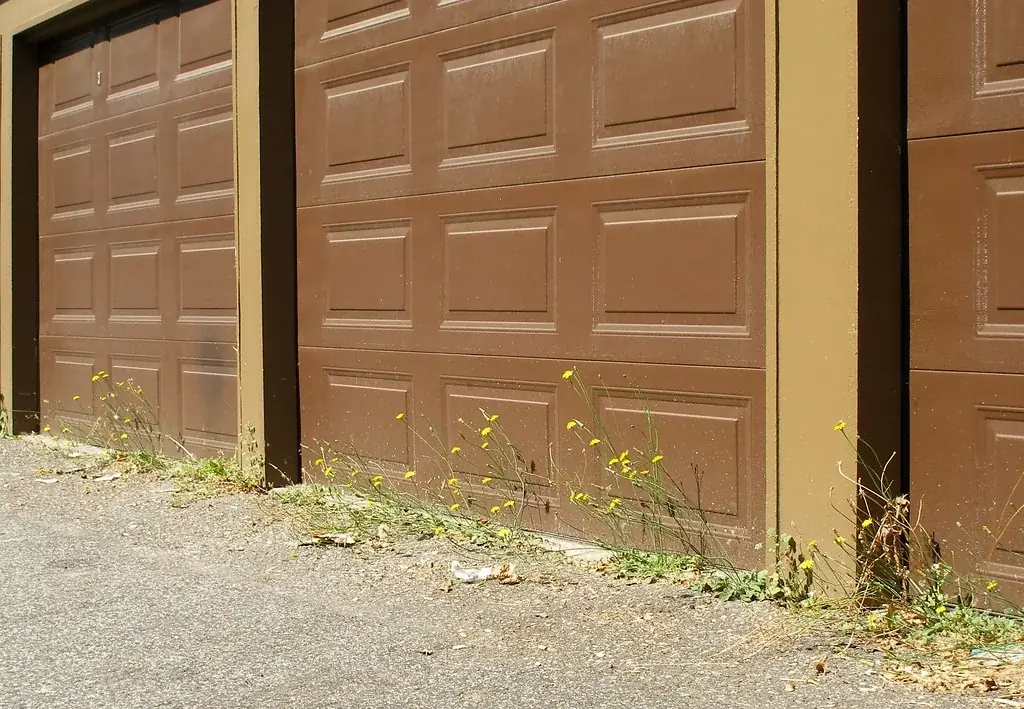 brown raised-panel garage doors on a gravel lot