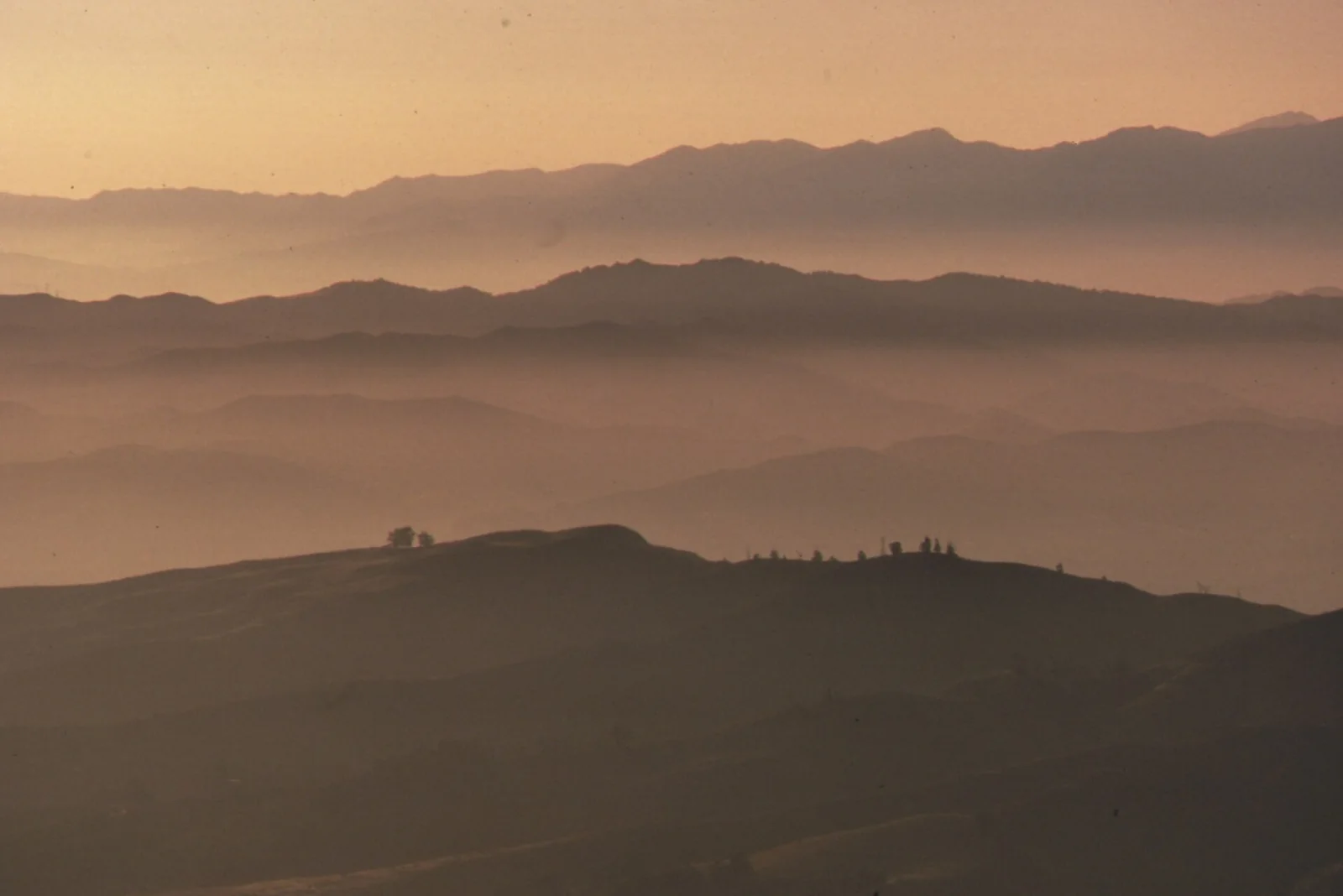 morning fog lying in layers over low hills under a pale sky