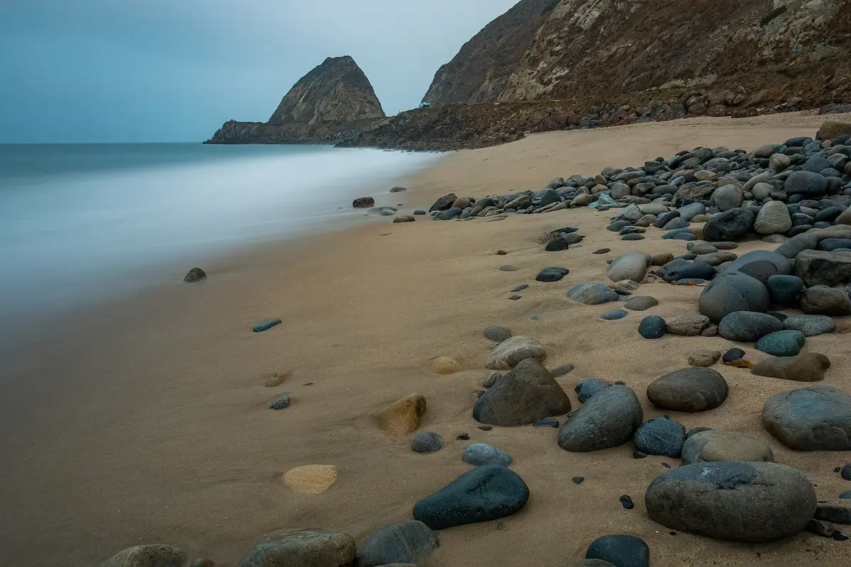 a rocky beach at low tide below a dark headland