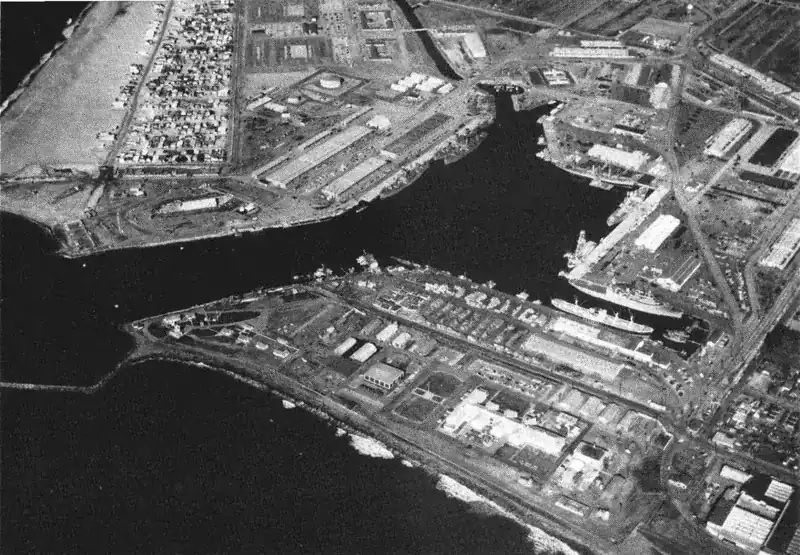 black and white aerial photograph of a deep-water harbor with piers and buildings