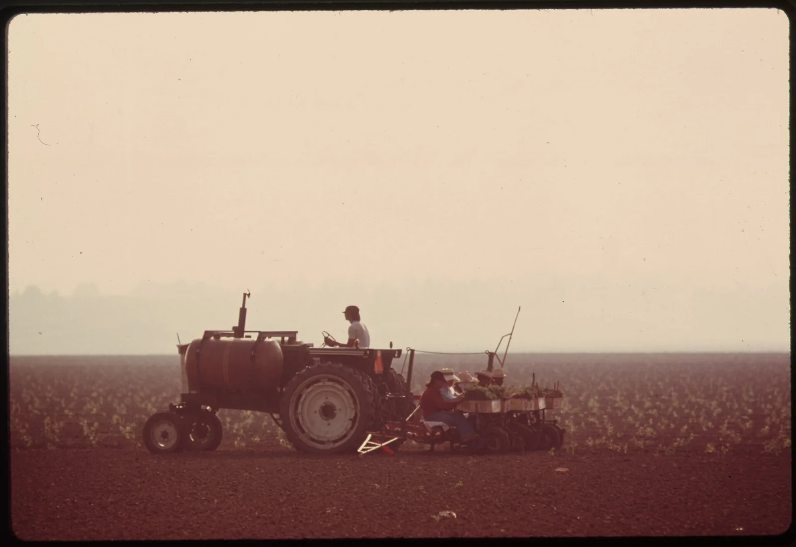 a farmer driving a tractor across a flat, hazy field